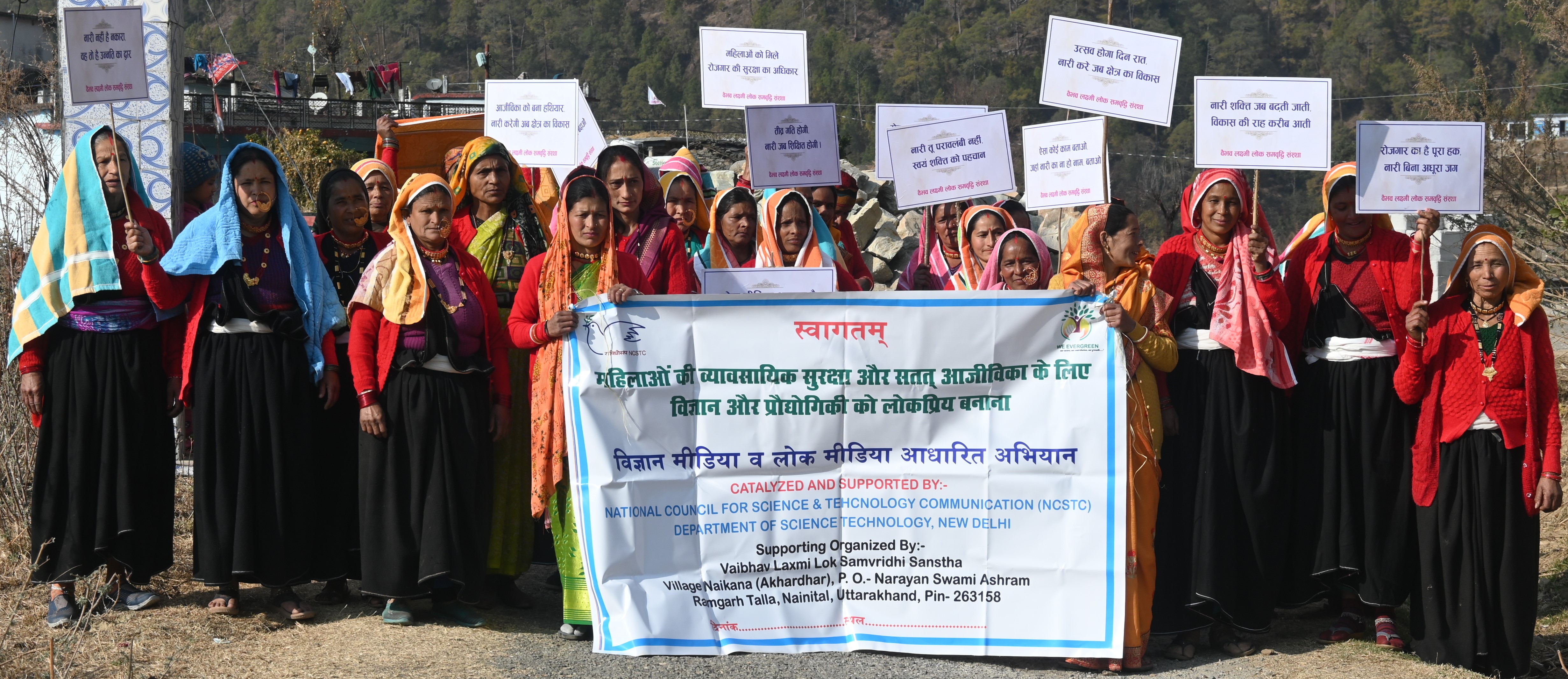 Community participants hold awareness placards and a science and folk-media programme banner.