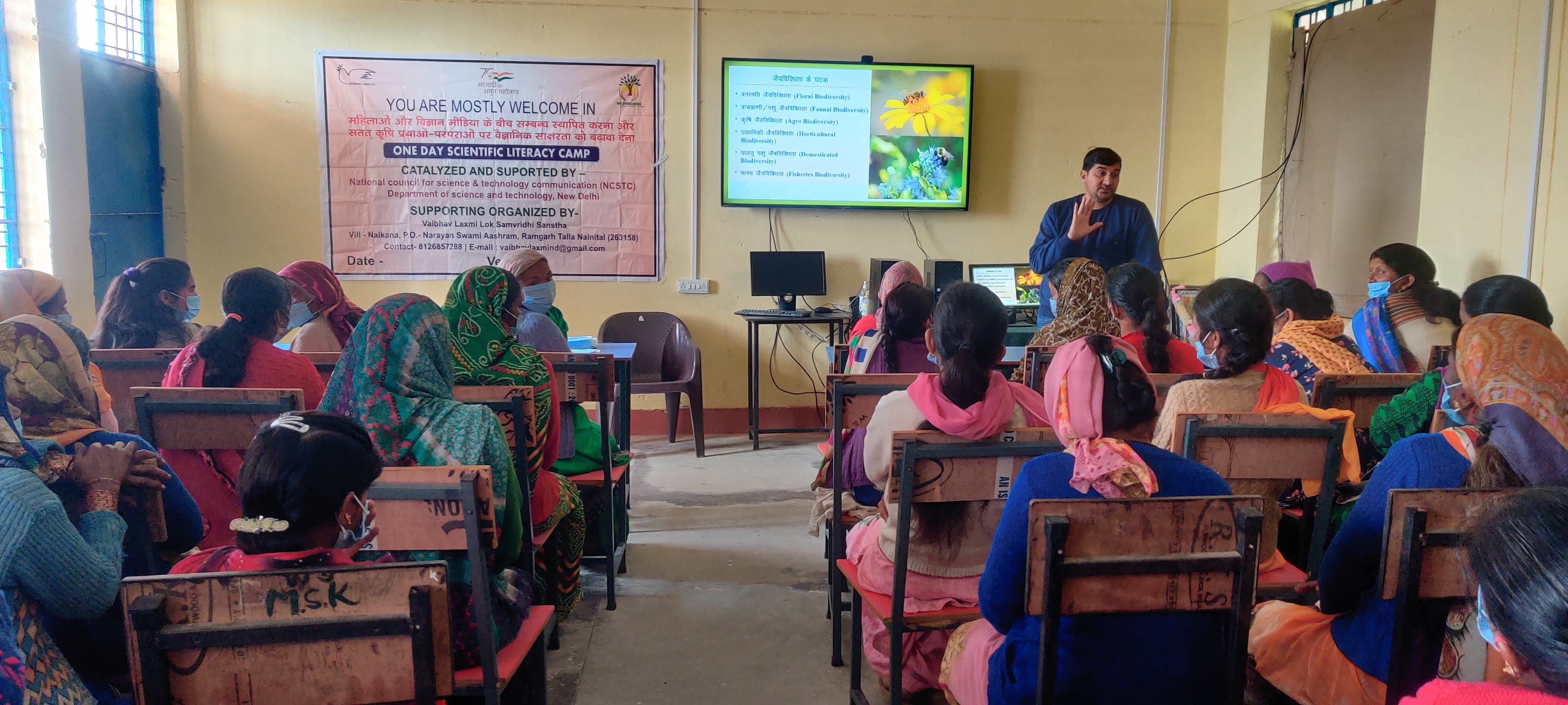Women sit at classroom desks while a speaker leads a workshop.