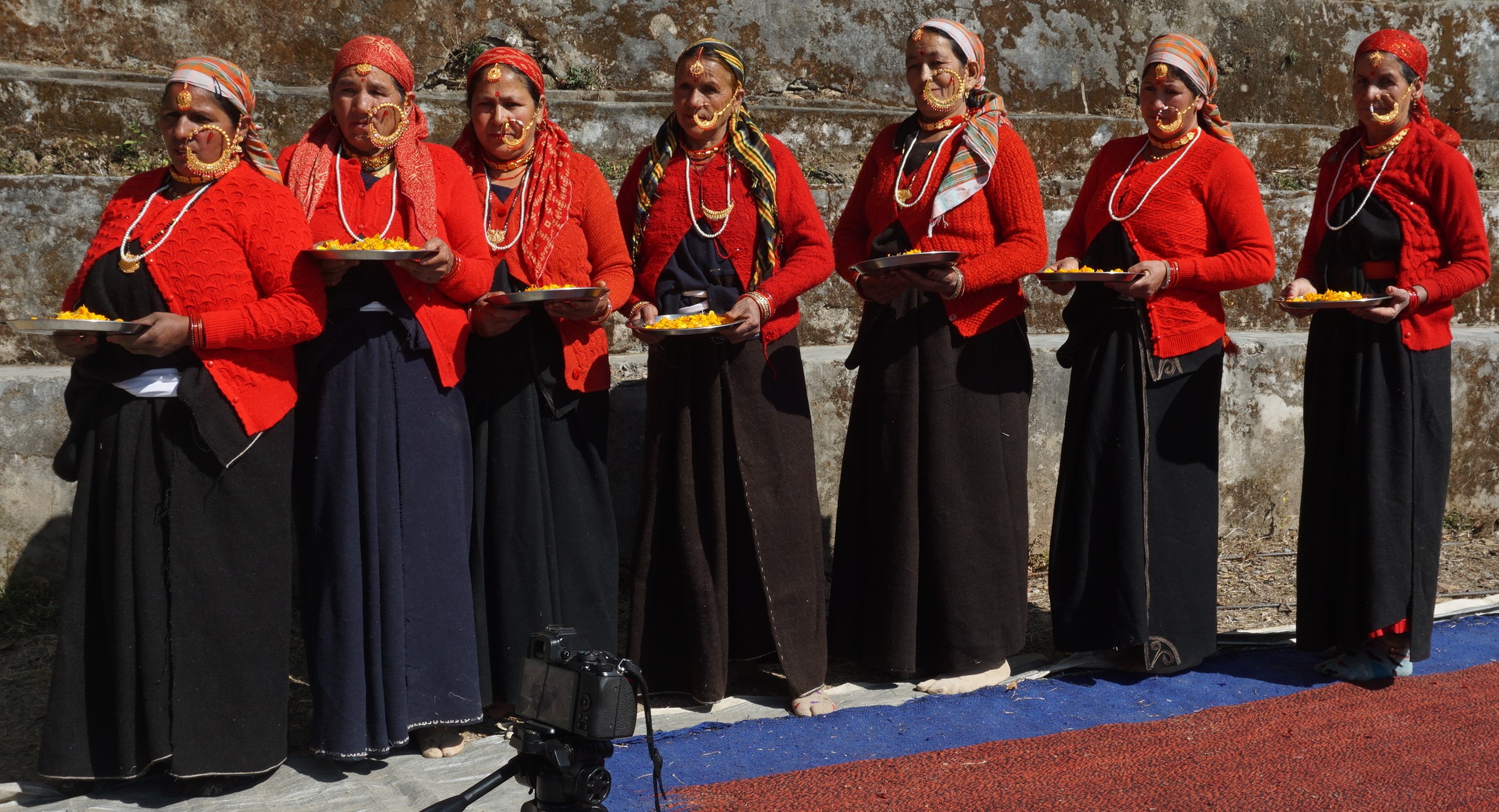 Women in traditional red and black clothing and jewellery stand together at Kaflodi.