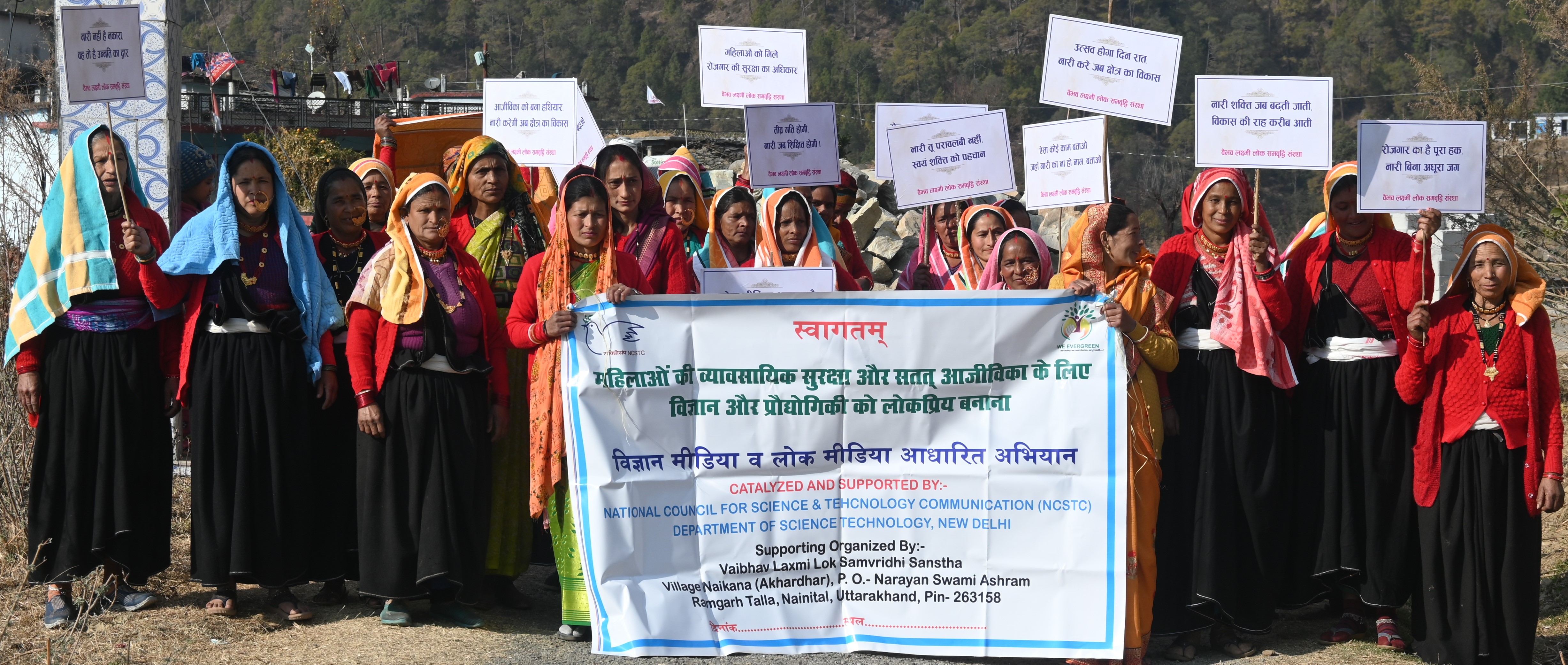 Women gather at Sankote holding awareness placards and a programme banner.