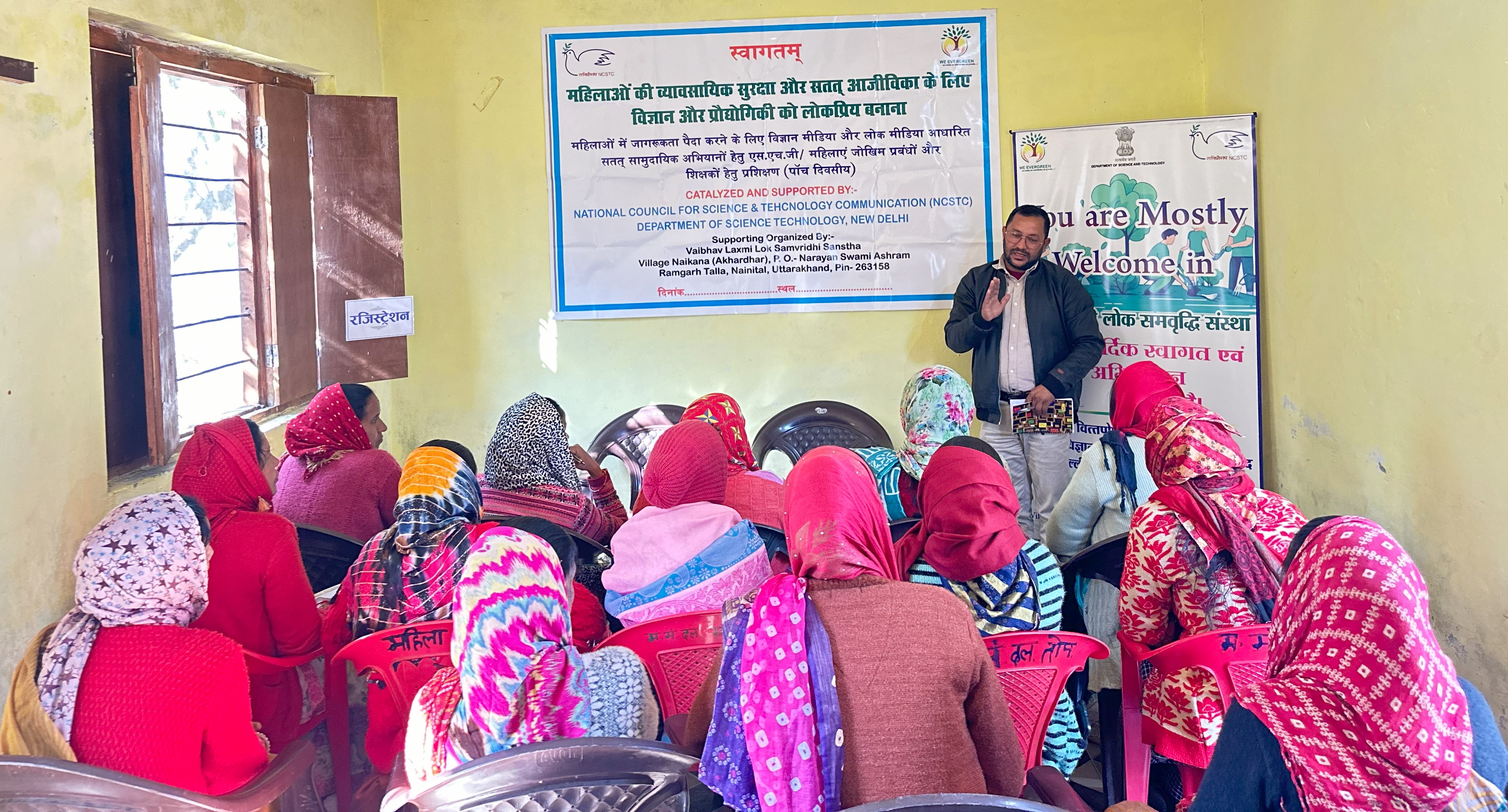 A speaker leads a livelihood training session for women seated in a workshop room.