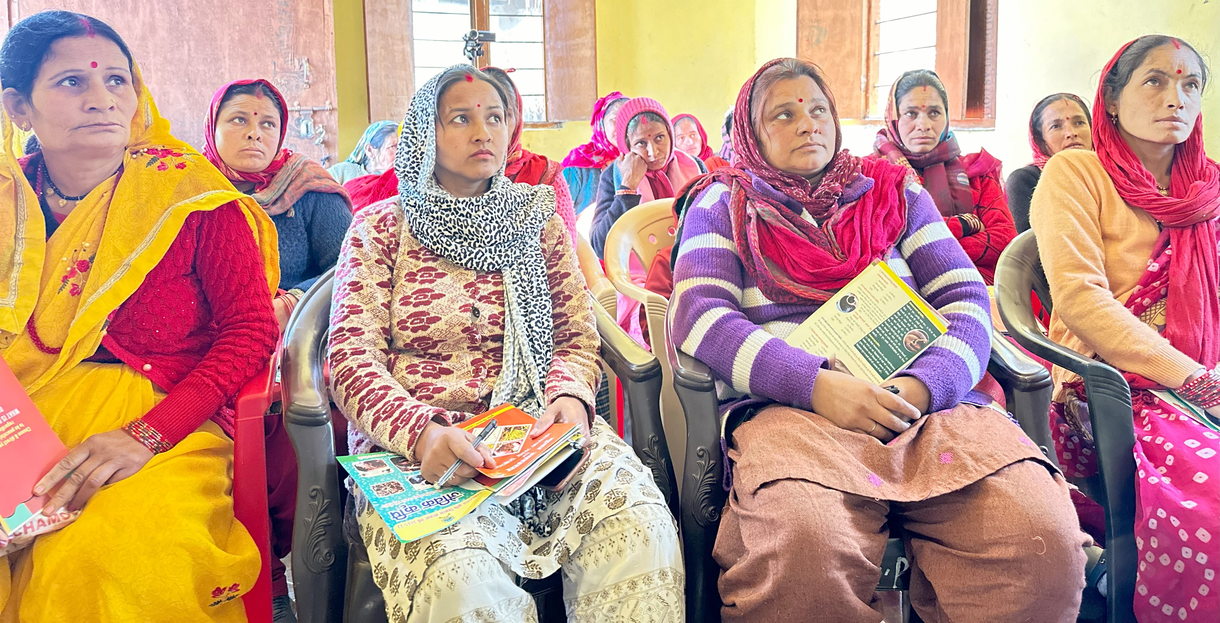 Women sit together and listen attentively during a community workshop.